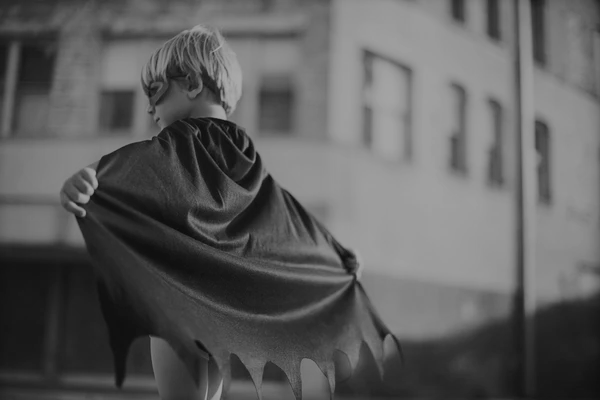 A black and white picture of a young boy wearing superhero costume.